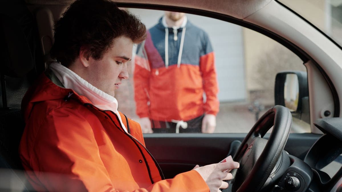 A delivery driver sitting in a car checking a job on a phone app