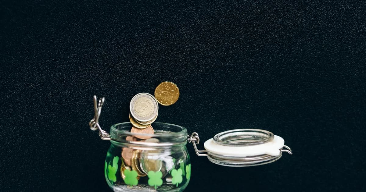 Glass jar with coins falling into it on a black background, symbolizing savings.