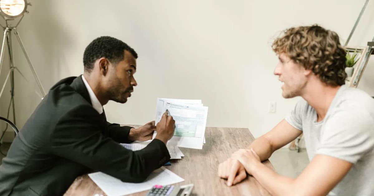 A financial advisor discusses paperwork with a client at a desk in a modern office.