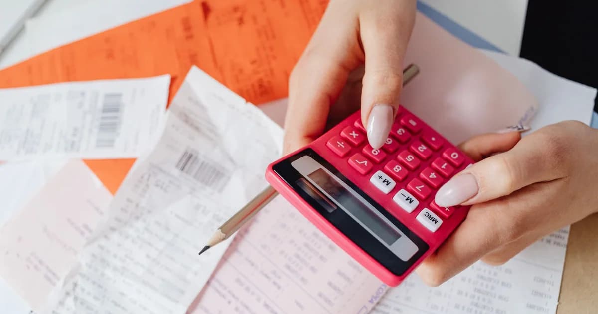 Hands using a pink calculator to manage expenses amidst various receipts and documents.