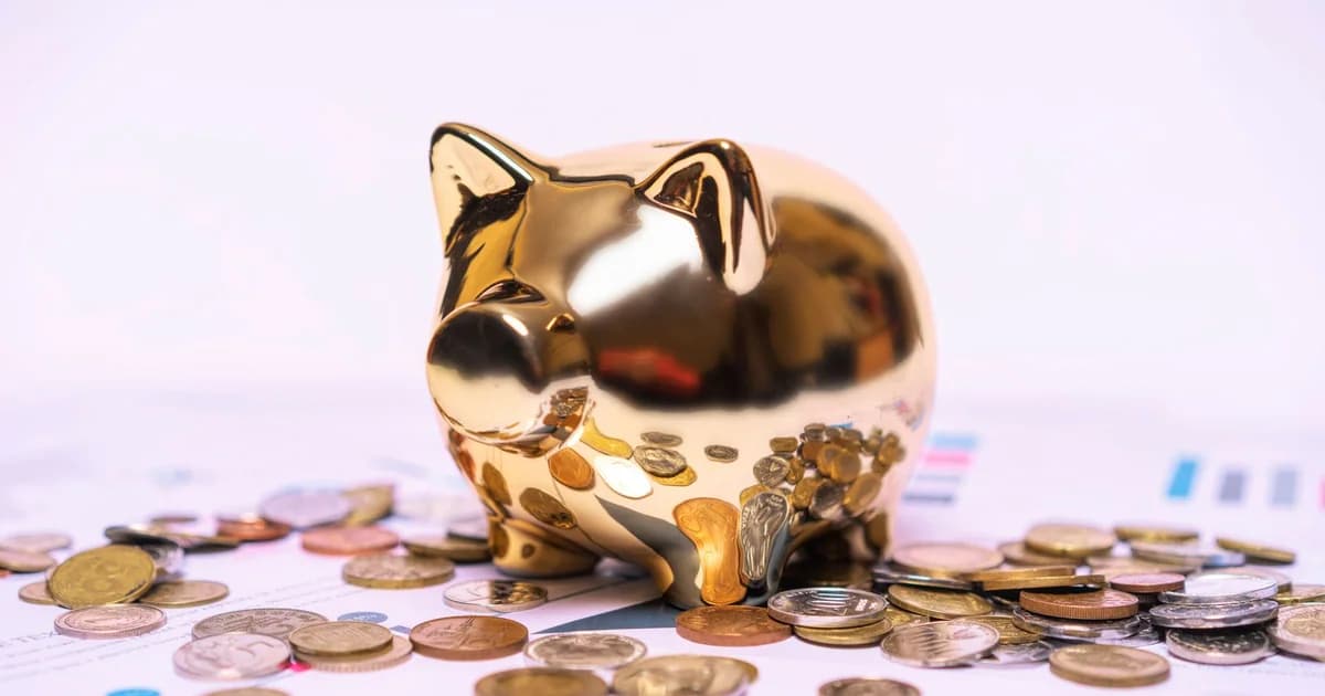 Shiny golden piggy bank on financial documents with scattered coins symbolizes savings.